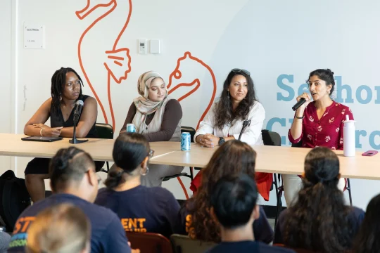 Four presenters seated at a table speaking to an audience at the Pier 57 Discovery Tank Classroom