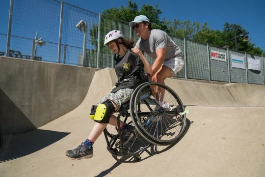 A person in a wheelchair and a guide rolling down a ramp at the Pier 62 Skatepark