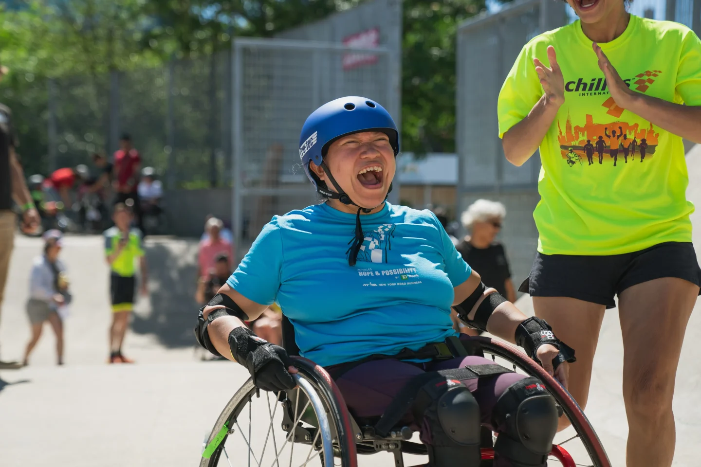 A person in a wheelchair pushes through the Pier 62 Skatepark while a guide cheers them on