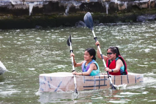 Two people paddling a cardboard kayak