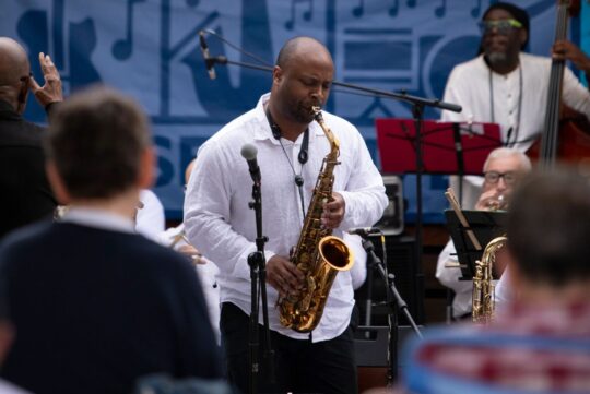 A saxophone player performs in front of an audience during a Jazz at Pier 84 concert