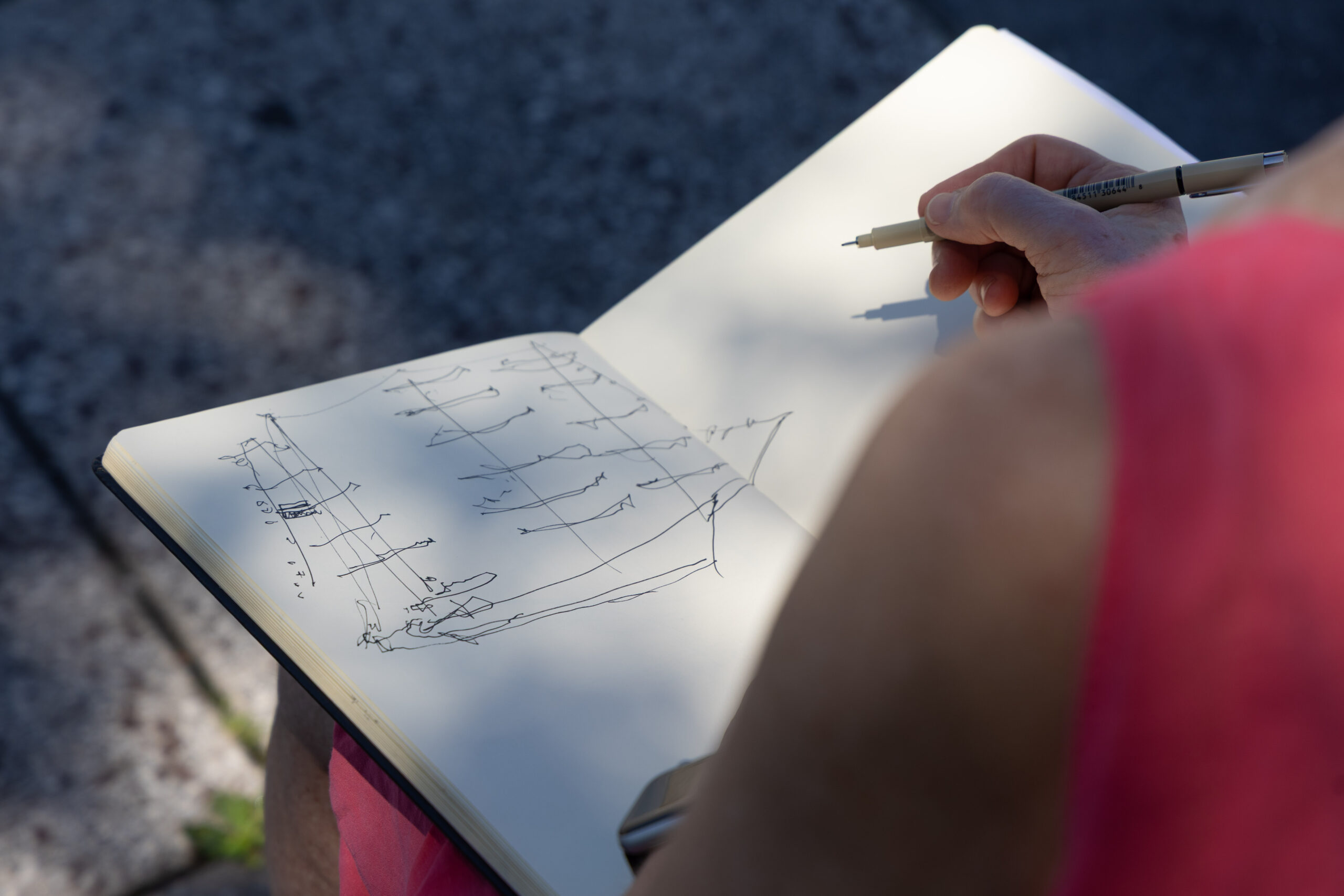 Person in red shirt drawing a ship in notebook