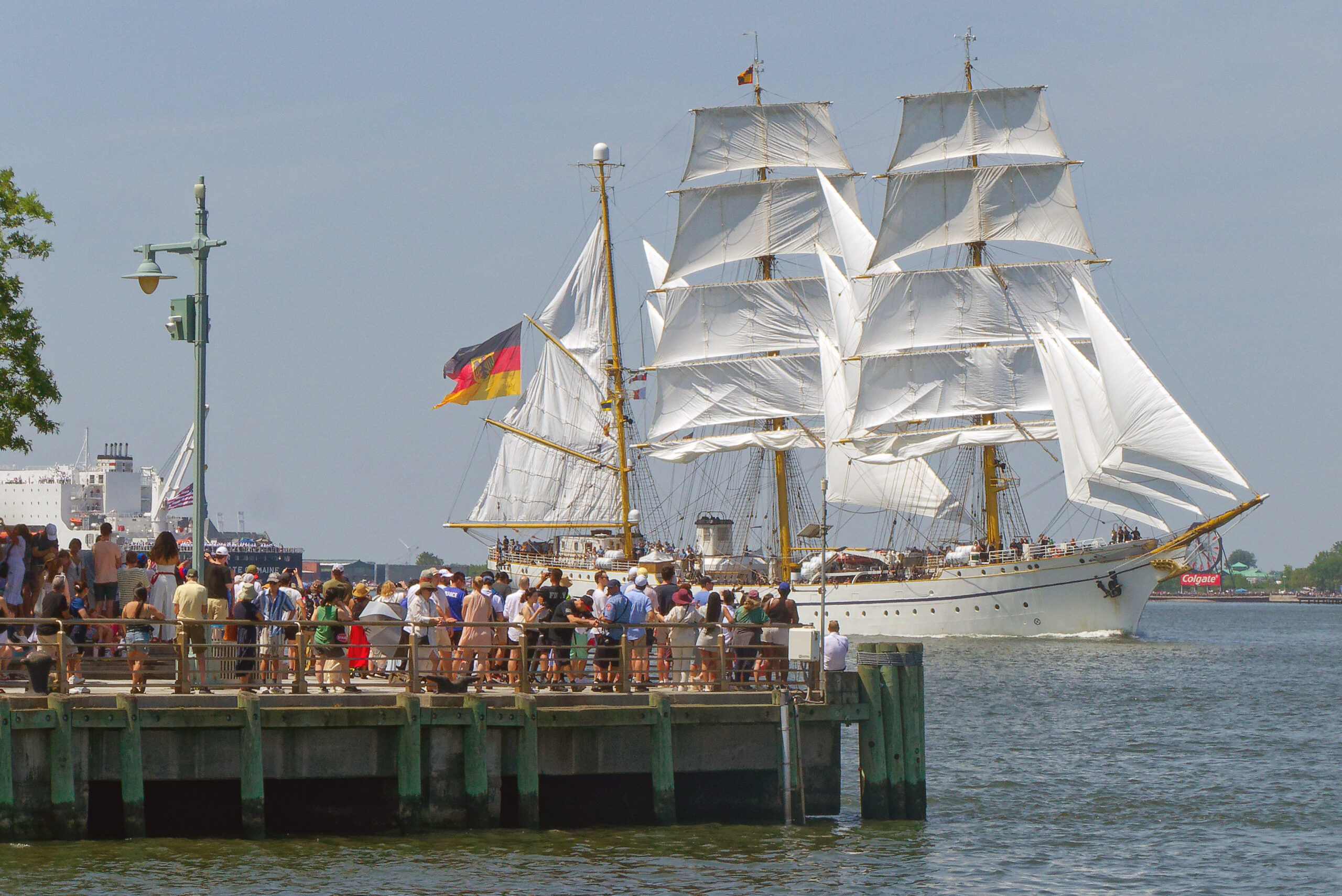 Crowds gather at edge of pier in Hudson River Park to view tall ship sailing by