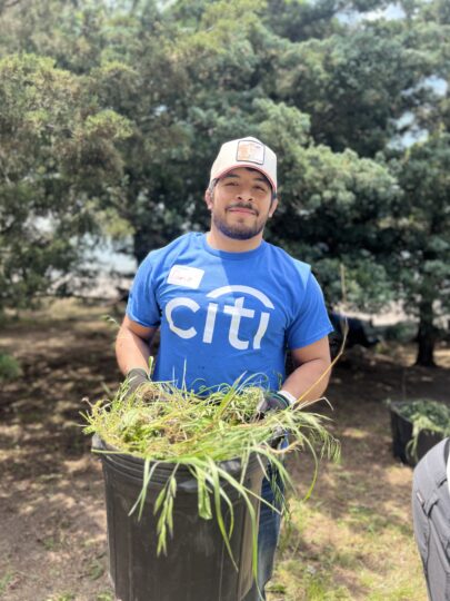 Citi volunteer holding a bucket full of trimmed plants