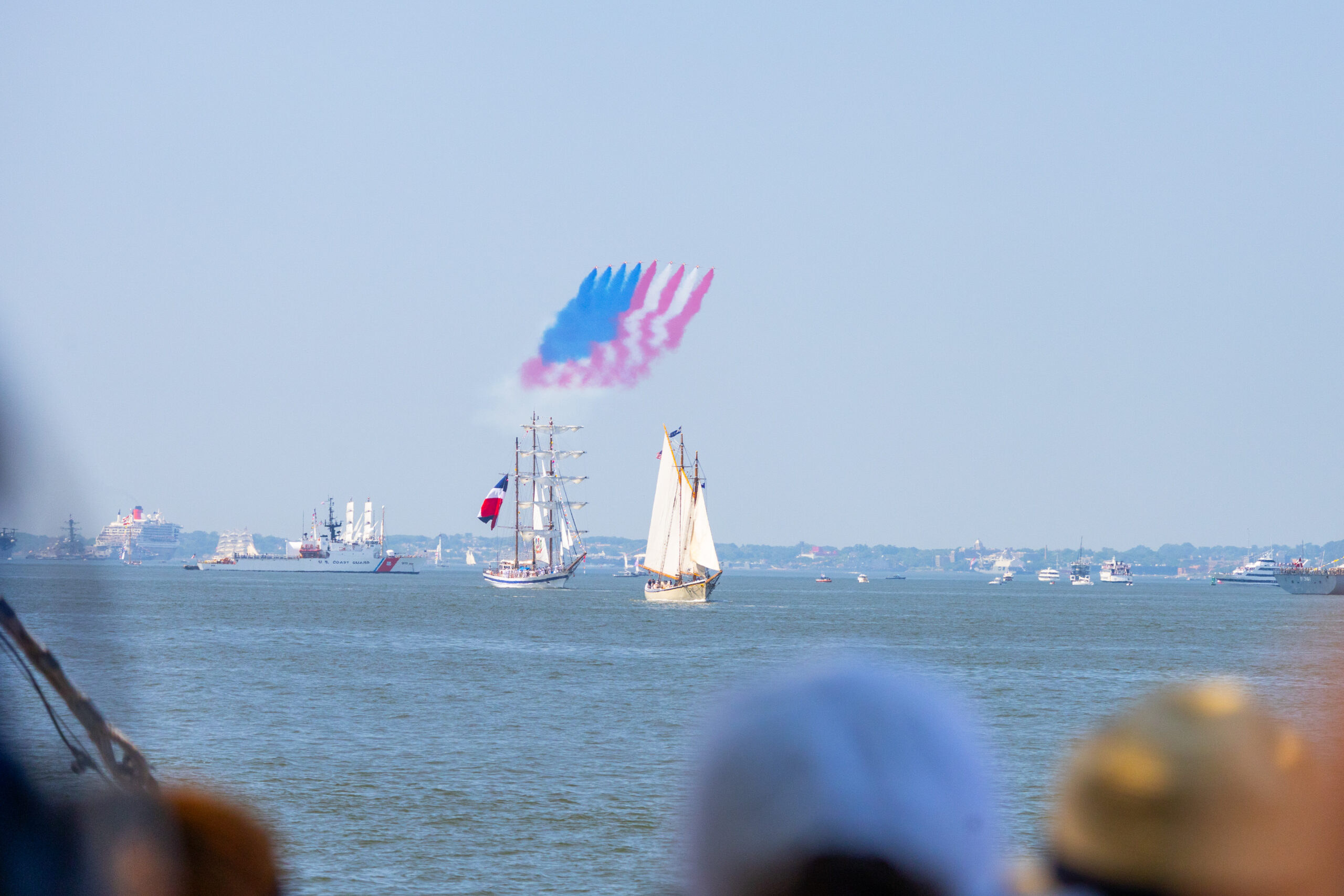 Tall ships sail into New York Harbor with red white and blue aerial display overhead