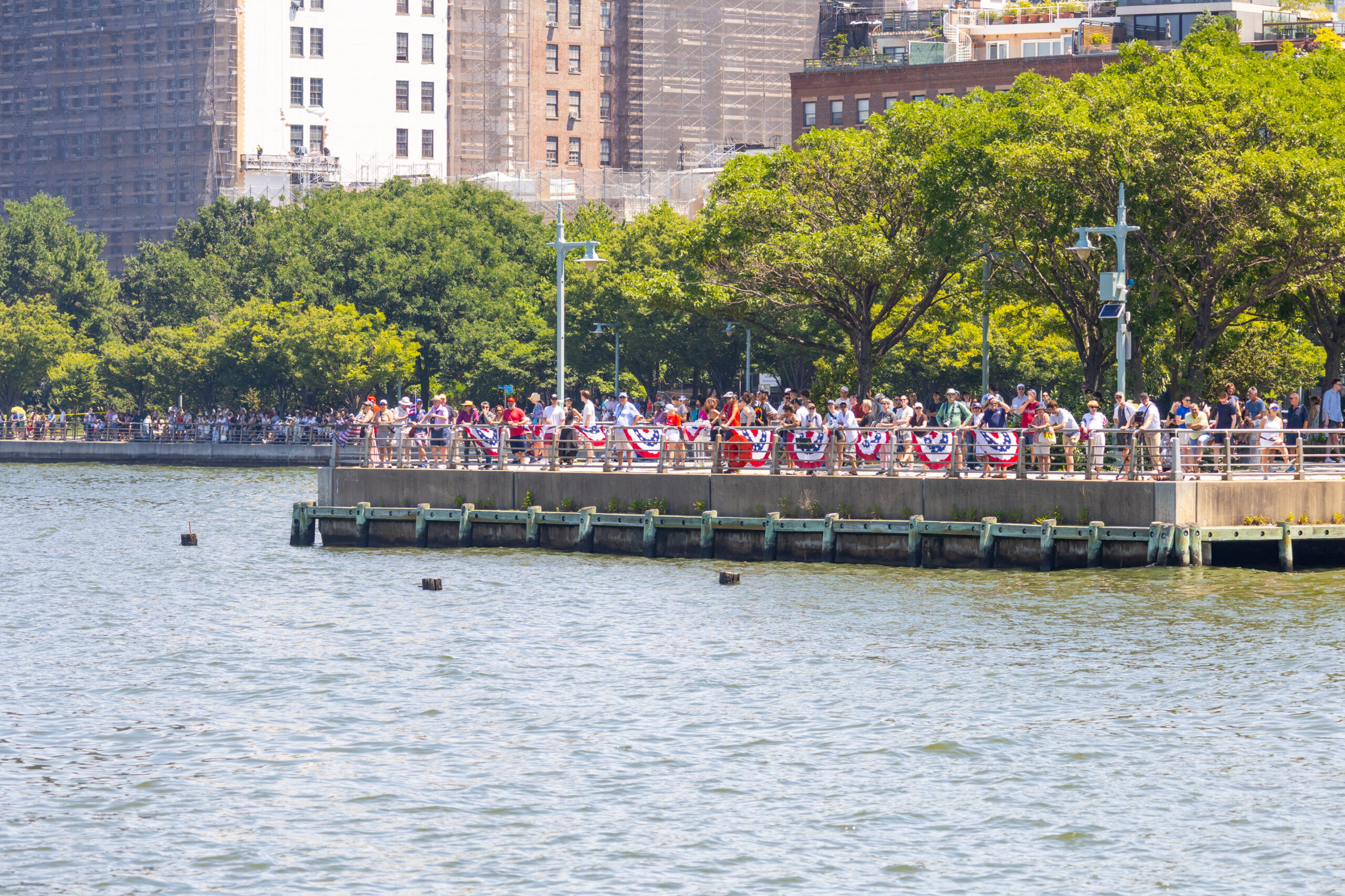 Crowds gather at Pier 46 in Hudson River Park, greenery and the city behind