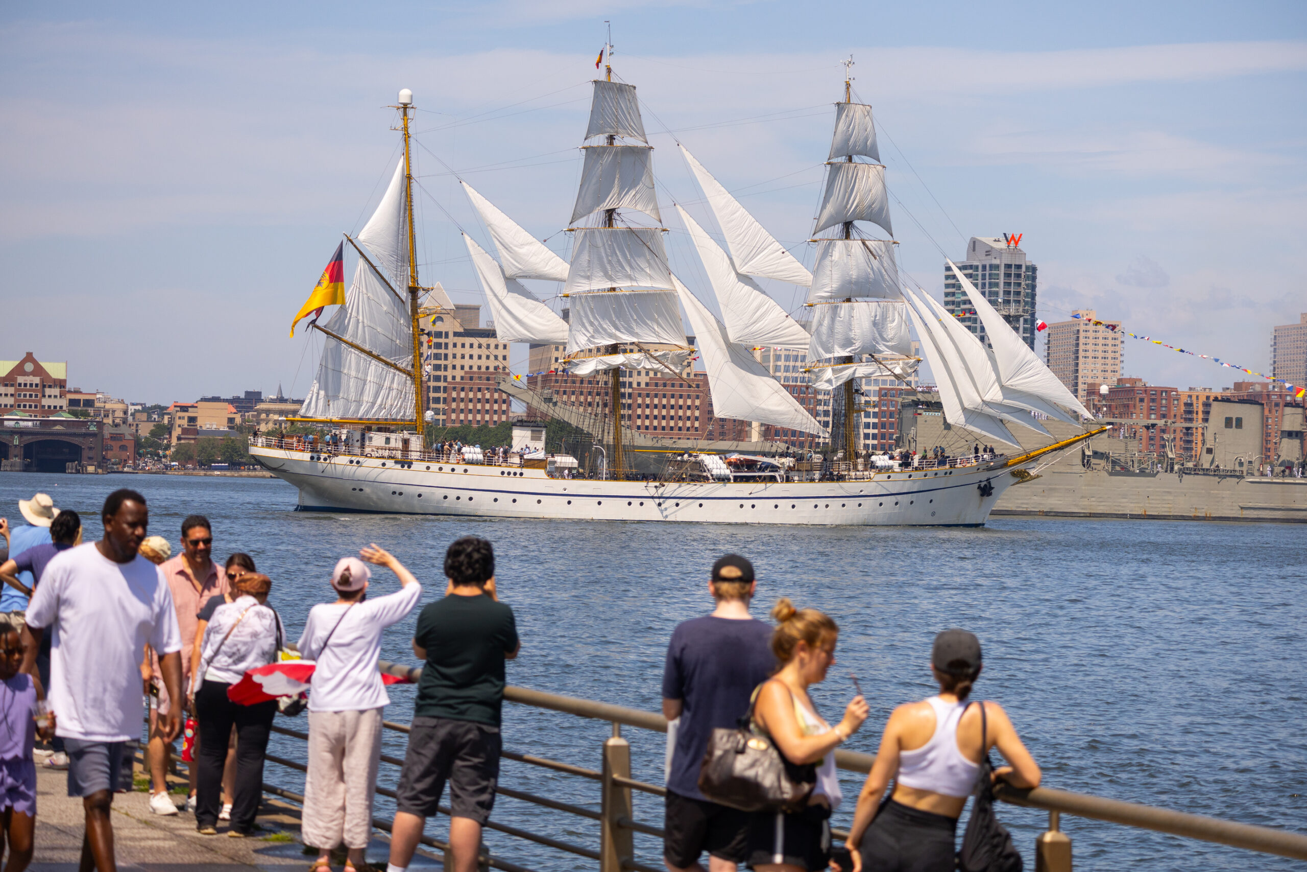 Tall ship sails by pier with people in Hudson River Park