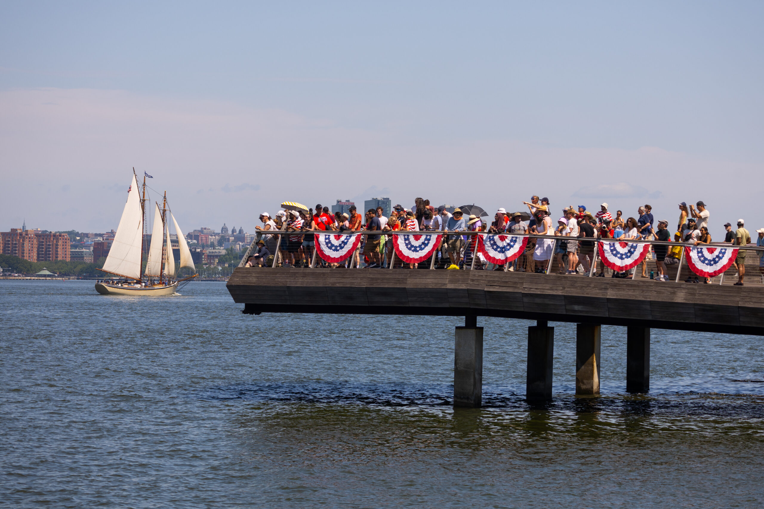 Crowds gather at edge of Pier 26 as sailboat sails by